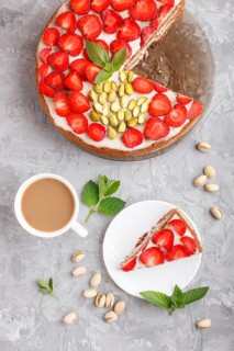 Homemade cake with yoghurt cream, strawberry, pistachio and a cup of coffee on a gray concrete