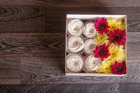 White box with white homemade zephyr and sunflowers and chrysanthemums on gray wooden background.