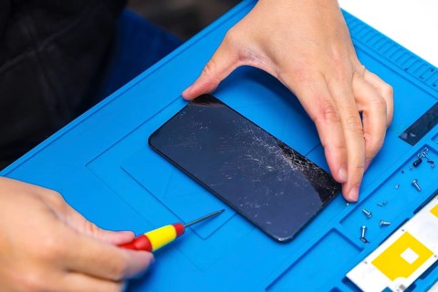 Close-up top view of a male technician uses a screwdriver to open the screen of a mobile phone in a