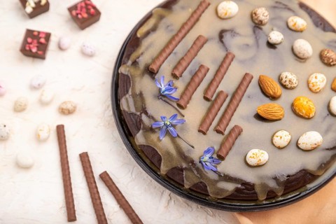 Homemade chocolate brownie cake with caramel cream and almonds with cup of coffee on a white
