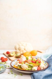 Vegetarian salad of cauliflower cabbage, kiwi, tomatoes, microgreen sprouts on white wooden