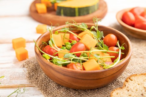 Vegetarian vegetable salad of tomatoes, pumpkin, microgreen pea sprouts on white wooden background