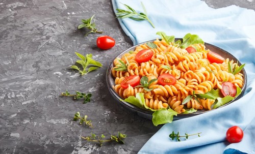Fusilli pasta with tomato sauce, cherry tomatoes, lettuce and herbs on a black concrete background