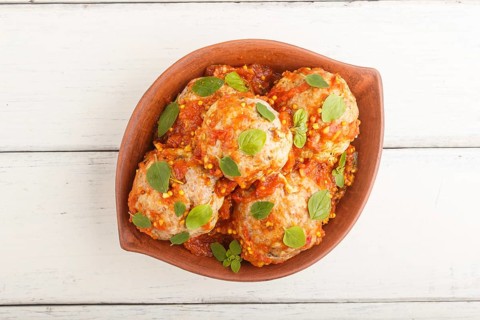 Pork meatballs with tomato sauce, oregano leaves, spices and herbs in clay bowl on a white wooden