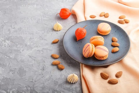 Orange macarons or macaroons cakes on blue ceramic plate on a gray concrete background and orange