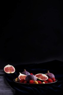 Fresh figs, strawberries and raspberries on blue ceramic plate on black concrete background and