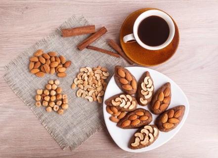 Small cakes potatoes with almonds and cashew nuts on a dessert plate. A cup of coffee, cinnamon,