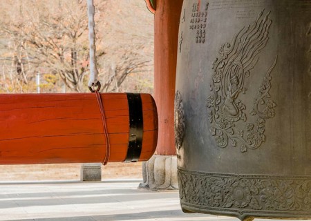 Large red wooden gong on linen wrapped chain hanging next to traditional metal Buddhist temple bell