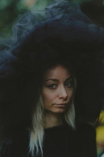 A woman wearing a tulle hat appears thoughtful, captured outdoors in natural lighting