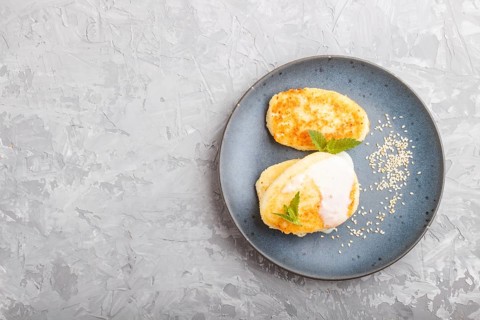 Cheese pancakes on a blue ceramic plate with milk sauce on a gray concrete background. top view,