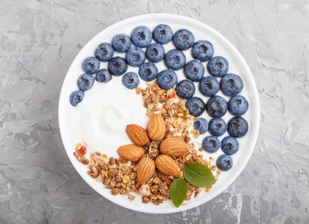 Yoghurt with blueberry, granola and almond in white plate on gray concrete background. top view,