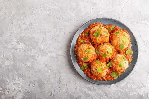 Pork meatballs with tomato sauce, oregano leaves, spices and herbs on blue ceramic plate on a gray