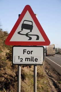 Red triangular road sign warning of slippery road surface ahead for half a mile, UK