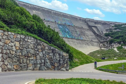 View from road pass road alpine road to road level below in front of outside of large dam wall of