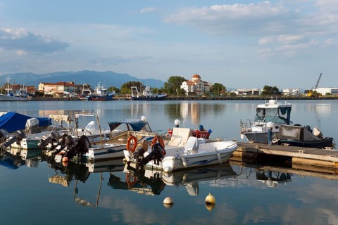 Motorboats are moored at a small jetty in a quiet harbour with a mountain panorama in the