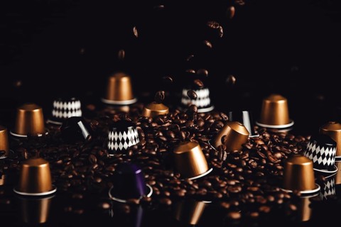 Scattered coffee capsules and coffee beans with falling coffee beans on a dark background