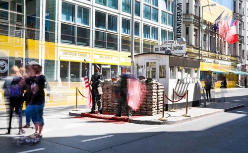 A long exposure shows a tourist at Checkpoint Charlie, men in American military uniforms stand in