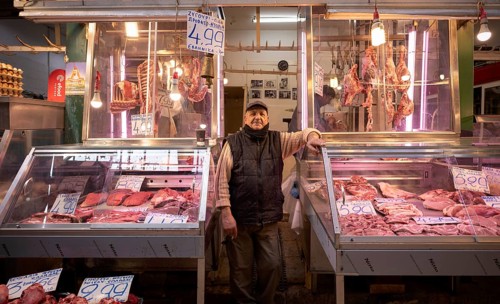 Butcher, meat trader posing proudly in front of his market stall, display of fresh meat, butchery,
