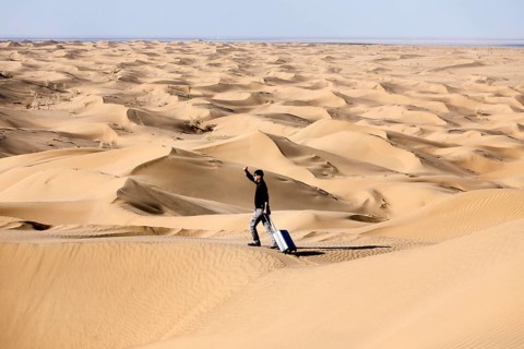 Symbolic image, tourist with suitcase in the desert, Mesr Desert, Iran. The Mesr Desert is part of
