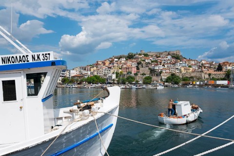 A boat in the foreground with a view of a hillside town by the sea under a partly cloudy sky, Old
