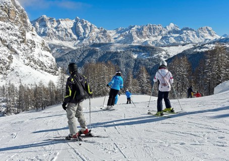 Skiers on a piste in front of the snow-covered mountain range of the Dolomites, winter sports