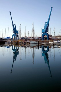 Two large blue industrial cranes reflected in water of Wet Dock marina, Ipswich, Suffolk, England,