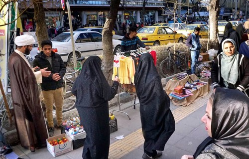 A mullah talks to a street vendor in Arak, Iran, woman wearing chadors and traditional dress on 16