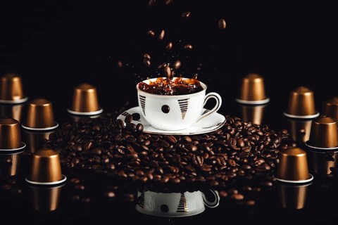 Coffee cup on coffee beans with falling beans and splashes, coffee capsules, reflection, black