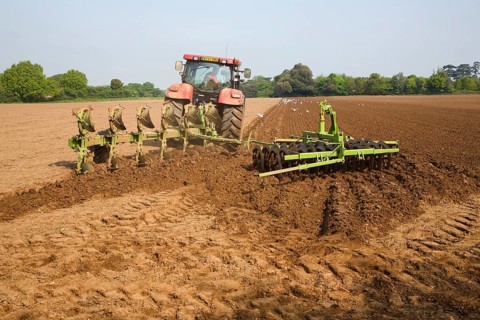 Tractor harrowing soil in field in preparation for planting, Shottisham, Suffolk, England, United