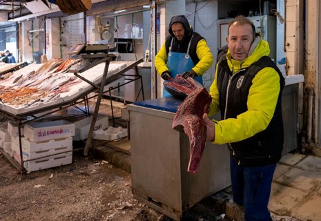 Trader, fishmonger posing proudly in front of his market stall, showing sliced tuna, display of