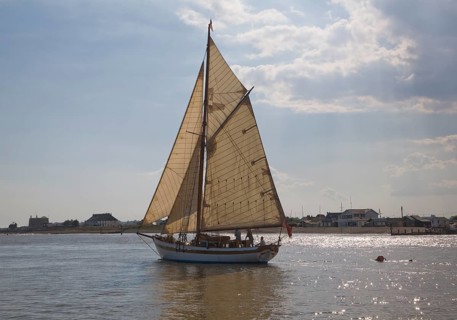Historic wooden sailing yacht boat in full sail at the mouth of River Deben, looking over to