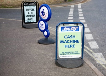 ATM sign outside shop with newspaper headline warning of scam taking place, Suffolk, England,