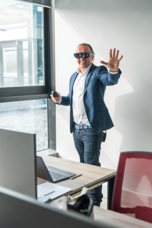 Vertical photo of a casual businessman gesturing using new mixed reality goggles in the office