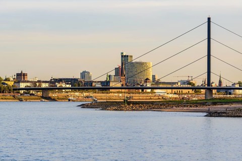City scene with bridge and buildings on the riverbank under a clear sky shortly in front of sunset,