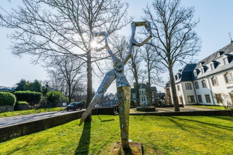 A modern metal sculpture in front of a castle, with the sun shining through its form, surrounded by