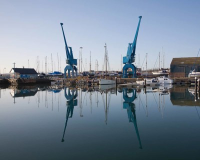 Two large blue industrial cranes reflected in water of Wet Dock marina, Ipswich, Suffolk, England,