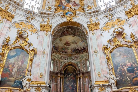 Interior view of a baroque church with richly decorated golden ornaments and ceiling frescoes,