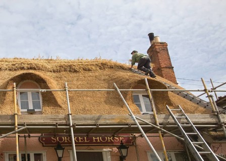 A thatcher completing the re-thatching of a traditional country pub, the Sorrel Horse, Shottisham,