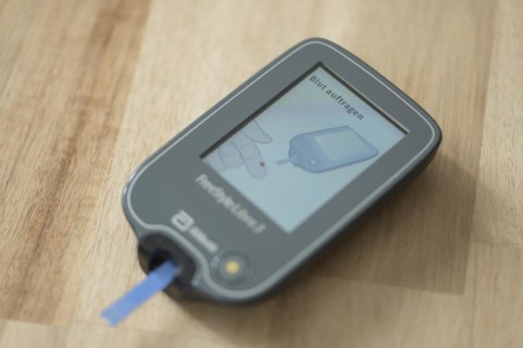 Blood glucose meter with test strips lying diagonally in the centre on a wooden table, ready for a