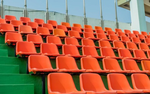 Rows of empty orange seats ascending green steps at a stadium, in South Korea