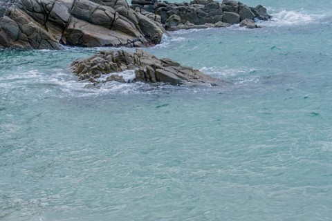 Foaming sea waves hit a rocky coast with a hint of green in the water, in South Korea