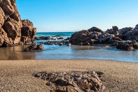 Sandy beach with large rocks and waves crashing in from the sea under a blue sky, in South Korea