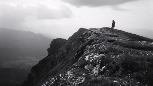 A hiker stands on a mountain peak surveying the surrounding rugged terrain, AI generated