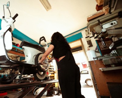 A focused female mechanic is at work on a scooter's tire in a workshop setting, latino woman in