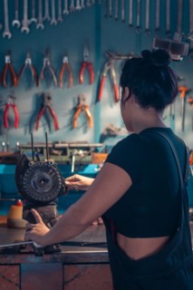 Female hispanic Mechanic working at a bench in a well-equipped workshop from behind, a complete