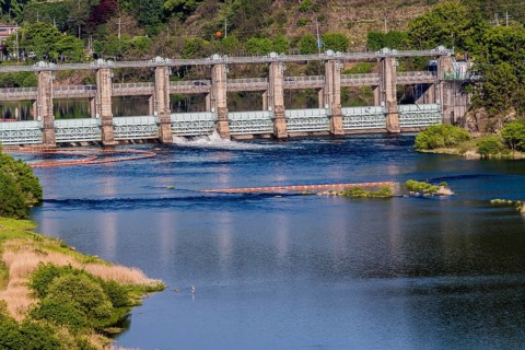Landscape of dam releasing water through one floodgate into river with blue water located near