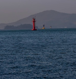 Three small lighthouses in a harbor with small mountains shrouded in fog and mist in the background