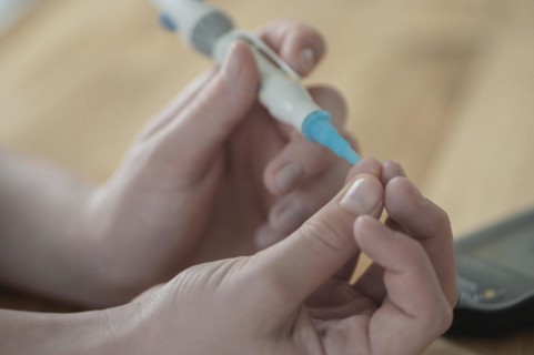 On the left a child's hand holding a lancet, lancing device, and pricking itself to determine the