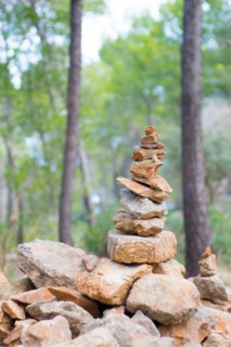 Carefully stacked, slightly red stones form a stone figure, cairn, waymark, marker, sparse pine