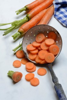 Carrot slices in colander and wooden spoon, Daucus carota